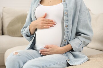 Pregnant woman touching her belly on sofa at home, closeup