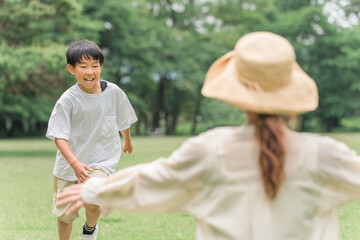 芝生の公園で手を拡げるママの元に走る男の子・親子（抱き合う・受け止める・愛情・ふれあう）
