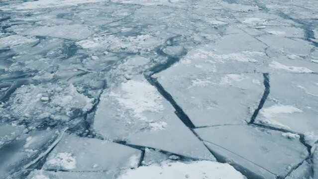 Flying over thick ice on top of a frozen lake during the middle of winter.