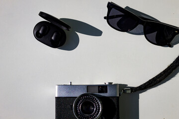 Wireless headphones, sunglasses and a film camera on a white background