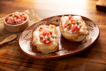 Molletes. Mexican recipe based on bolillo bread split lengthwise, spread with refried beans and gratin cheese, adding pico de gallo sauce and some protein such as ham, bacon or chorizo.