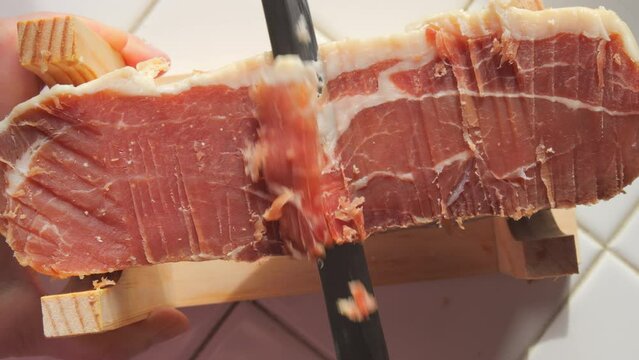 Spanish traditional pork jamon. A knife cuts a piece of hamon meat into thin slices in the kitchen, top view
