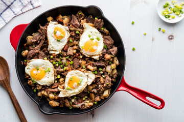 Delicious roast beef hash in a frying pan topped with fried eggs.