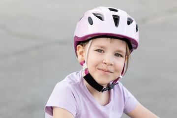 Smiling happy young child, a girl wearing a pink safety helmet with straps fastened, kid cyclist biker portrait, face closeup, outdoor activities, one person, real people lifestyle shot, childhood