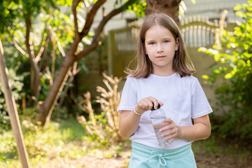 Young girl, child holding a clear transparent modern reusable water bottle outdoors on a sunny day. Hydration, children drinking water and staying hydrated simple concept, copy space, one person