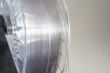 A spool of silver transparent high quality 3D printing filament is positioned for use over a...