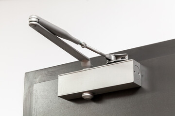 Close-up showing a modern silver door closer mechanism, with its hydraulic arm extended, installed...