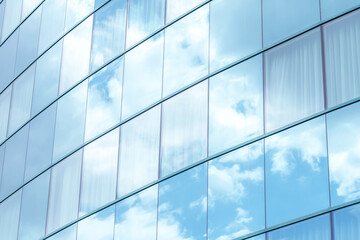 Contemporary office building with reflective glass panels that mirror blue sky and white clouds,...