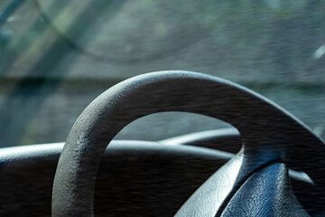 Extreme close-up of a section of a steering wheel and part of the dashboard of a vehicle, taken from the drivers seat perspective. Sunlight filters through the windshield, generic car interior detail
