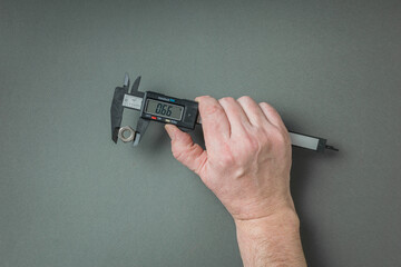 A man's hand with an electronic caliper on a gray background.