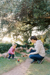 Smiling mother squatting near little girl pushing wheeled toy