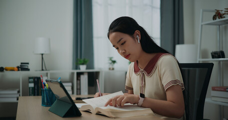 Selective focus, Side view, Female wireless headphones writer sitting at desk writing information...