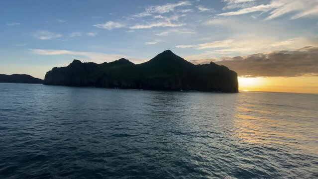Tiny island with town in Southern part of Iceland during sunset, view from sailing vessel