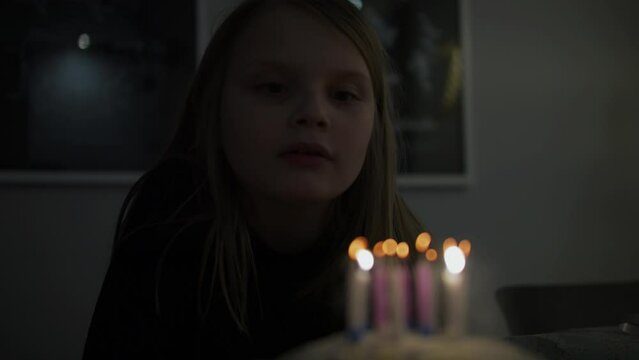 Close up static shot of birthday girl blowing candles in dark room