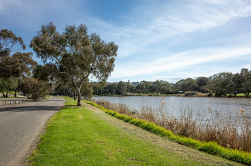 Scenery of the riverbank of Barwon river in Geelong, Australia. Background texture of serene landscape with road bordered by grass, peaceful river meanders alongside.