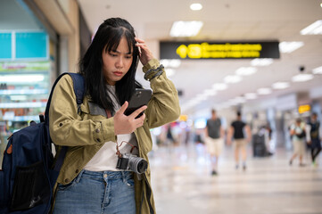 A confused female is reading her flight information on her phone with a serious, doubtful face.