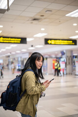 A happy Asian female solo traveler is walking in the airport, looking for her check-in counter.