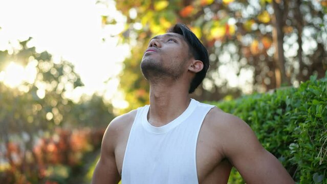 Young Asian man with a strong body, trail running, running in the morning summer sunshine, exercising, body breathing in and out. Warm up before running for health and live a healthy life.