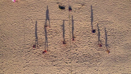 Aerial view. Tourists play beach volleyball at sunset. The shadows of the players create interesting figures in the sand. Beach sports