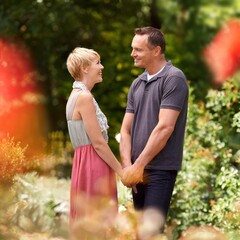 Happy, holding hands and couple in a park with love, trust and support, solidarity and security while bonding in nature. Commitment, care and people on a field of flowers for spring romance or date