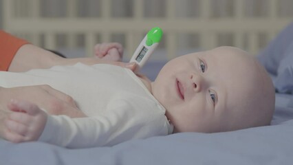 Cute Baby boy lying on back look at camera while temperature is taken with digital thermometer. Child Health care and medical check up concept. Pediatric theme for design and educational material.