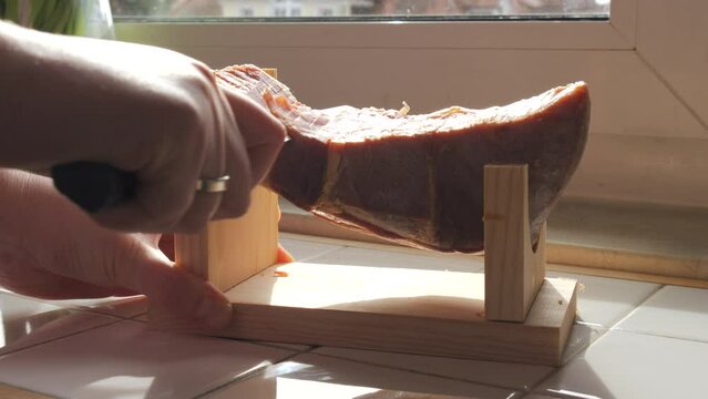 Spanish traditional pork jamon. A knife cuts a piece of hamon meat into thin slices in the kitchen