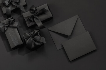 Black gift boxes with satin bows and a black envelope on a black background with space for text....