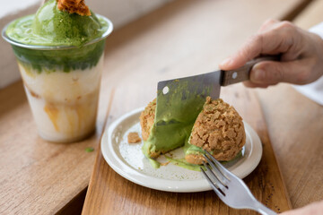Close-up of a woman eating a green tea cake with a fork and knife at a wooden table