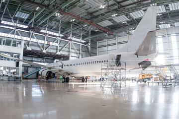 White passenger airliner in the aviation hangar. Airplane under maintenance. Checking mechanical...