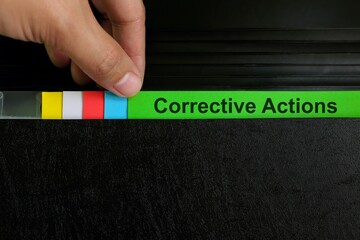 Hand picking corrective action file organizer in black background. Audit findings and root cause...