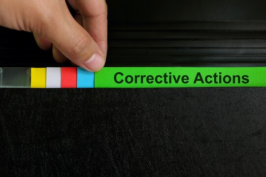 Hand picking corrective action file organizer in black background. Audit findings and root cause analysis concept.
