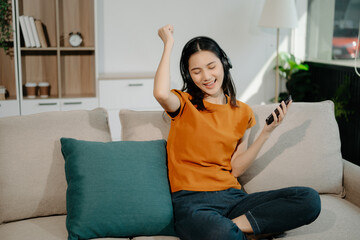 Young asian woman using smartphone and tablet while seated on couch at home.