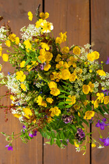 Bright colorful bouquet of wild flowers standing on wooden background with copy space, vertical botanical photo of yellow small flowers