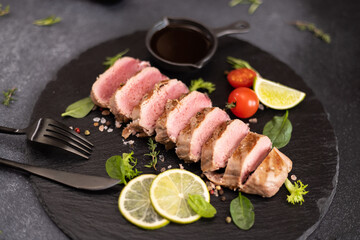 sliced grilled cooked piece of tuna fillet on black stone serving board