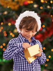 Happy, Christmas and boy child with present for celebration or surprise at festive party at home. Smile, santa hat and cute young kid opening a gift box for xmas event at modern house with decoration