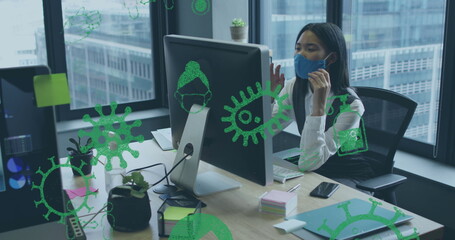 Image of virus icons over businesswoman with face mask using computer in office