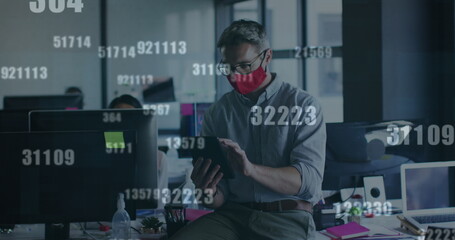 Image of financial data processing over businessman with face mask using tablet in office