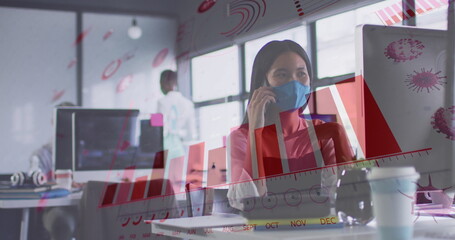 Image of financial data processing over businesswoman with face mask using smartphone in office