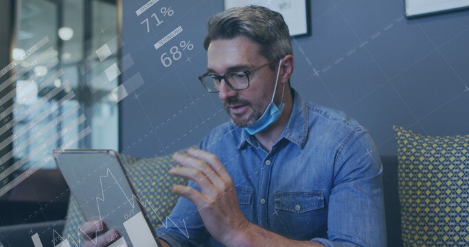 Image of financial data processing over businessman with face mask using tablet in office