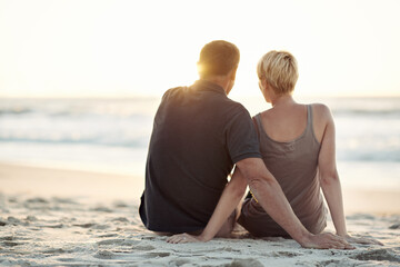 Nature, beach and back of couple at sunset for bonding, relax together and relationship by ocean. Dating, travel and man and woman hug, embrace and sitting on holiday, vacation and weekend for love