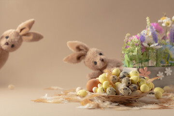Easter eggs, feathers, spring flowers, and toy bunny on a beige background.
