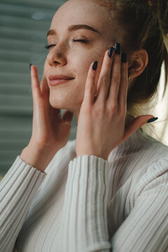 Beautiful young lady touching face enjoying healthy soft moisturized hydrated facial skin. Everyday treatment concept.