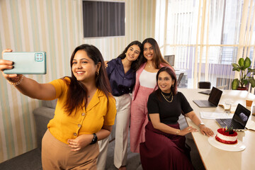 Woman taking selfie with her colleagues during birthday celebration in office 
