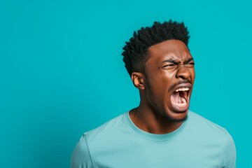 Obraz premium 26-year-old African American man, his stance aggressive, lips curled in a snarl, reacting to a confrontation on the street, captured against a solid pastel turquoise background.