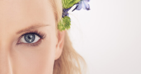 Woman, flowers and half face in studio with beauty, makeup or cosmetics with eyelash extensions on...