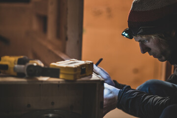 Close-up of Man preparing to drill in wood in low light with headlamp
