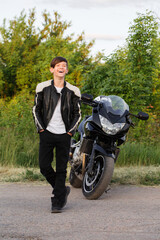 Fototapeta na wymiar A teenage boy laughs cheerfully near a motorcycle