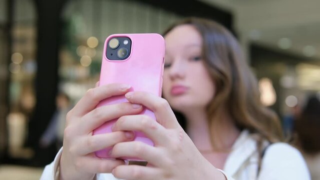 young girl in the Mall takes a selfie, straightens hair, photographs herself, makes eyes, pouts her lips, smiles, adolescence, shows off in front of the camera, films herself, makes short videos