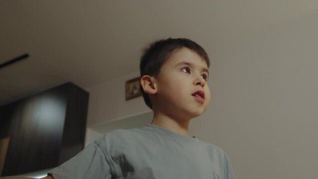 Caucasian little boy with brunette hair in a t-shirt gesticulating with his hands, playing alone at home. Caucasian man.