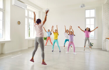 Smiling happy girls training modern dance moves together in studio with female choreographer. Group of kids doing dance workout in choreography class. Children sport and active lifestyle concept.